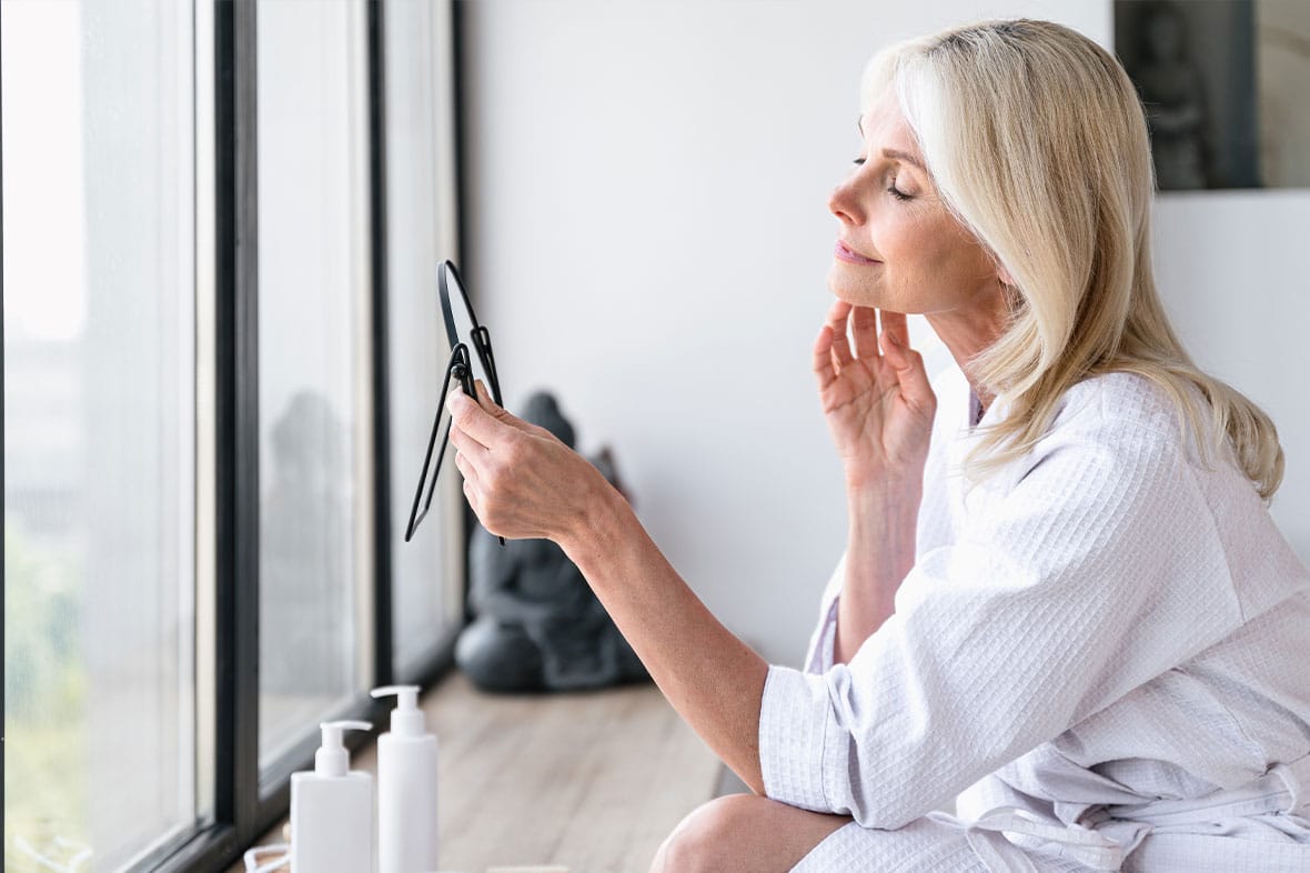 older woman looking in the mirror after her mini facelift in NYC